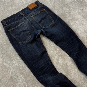 Nudie grim tim jeans - Tjena! Säljer dessa feta mörkblå Nudie ”Grim Tim” jeansen med najs tvätt! Jeansen är i fint skick, hsr ett väldigt litet hål i ena fickan (bild 5) men inget man märker av. Size 32/34 men lite små i storlek så skulle säga typ 31/32. Skriv vid funderingar!
