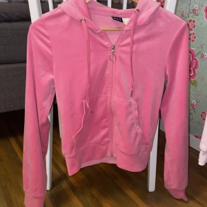 Rosa hoodie i velour från Gina Tricot - Supermjuk rosa hoodie i velour från Gina Tricot. Tröjan har huva med snörning, dragkedja framtill och två fickor. Perfekt för en chill och avslappnad stil. Långärmad och med ribbade muddar för extra komfort. En fläck som jag ej  fått bort i tvätten men syns knappt och går säker bort med lite medel magi! Nedsänkt pris 