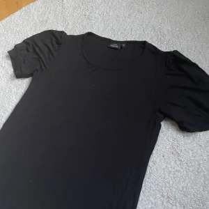 Svart ribbad topp från KappAhl - Svart ribbad topp från KappAhl i storlek S. Modellen har korta puffärmar och rund halsringning. Tunt och mjukt material som känns skönt mot huden. Perfekt att styla med jeans eller kjol för en clean look.