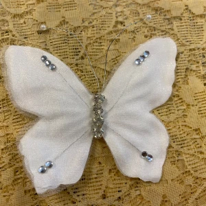 Vit fjäril Hårspänne med pärlor och strass - Superfin brosch i form av en vit fjäril med glittriga strasstenar och pärlor på vingarna. Tillverkad i ett tunt, skimrande tyg och har metalltrådsantenner med pärlor. Fästes enkelt med en metallklämma på baksidan. Perfekt för att piffa upp din outfit. Helt ny , finns fler kvar, samma frakt 