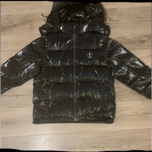 Svart pufferjacka från Trapstar  - Säljer en svart, glansig pufferjacka från Trapstar med huva och dragkedja framtill. helt ny Trapstar jacka använd 4 gånger bara, Och det funkar med bytte. 