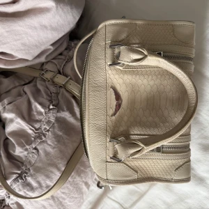 Beige handväska från Zadig & Voltaire - Säljer en beige handväska från Zadig & Voltaire i skinn med coolt ormskinnsmönster. Väskan har både handtag och justerbar axelrem, silverfärgade metalldetaljer och dragkedjor. Kvitto finns!