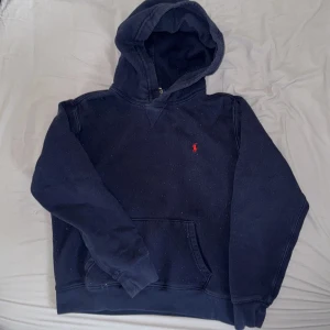 Mörkblå hoodie från Polo Ralph Lauren - Säljer en mörkblå hoodie från Polo Ralph Lauren med klassisk röd broderad logga på bröstet. Tröjan har huva och magficka, samt långa ärmar. Perfekt för en avslappnad och stilren look.