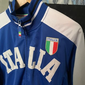 Vintage Italia track jacket - Säljer en blå och vit track jacket med 'ITALIA' tryckt på bröstet och Italiens flagga som emblem. Jackan har dragkedja, ståkrage och randiga muddar. Supersnygg men för stor på mig :(