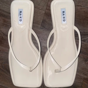 Vita sandaler med fyrkantig tå från NA-KD - Säljer ett par stilrena vita sandaler från NA-KD med fyrkantig tå och tunna remmar. Skorna har en liten klack och minimalistisk design, perfekta för varma dagar. Skorna är helt nya och är helt oanvända. 🌸💞