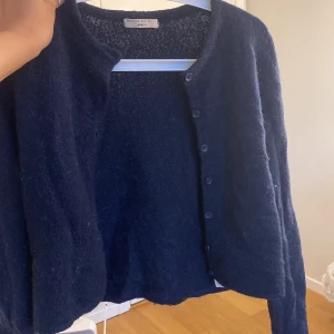 Mörkblå stickad kofta från Gina Tricot - Säljer en mörkblå stickad kofta från Gina Tricot i storlek S. Koftan har långa ärmar och är kortare nedtill samt knäppning framtill med flera knappar. 