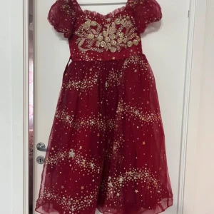 Röd balklänning med stjärnmönster och broderier - Magisk röd balklänning med puffärmar, glittrande stjärnmönster och vackra guldbroderier över bysten. Klänningen har en romantisk, vid kjol och är tillverkad i ett tunt, skimrande material som ger en sagolik känsla. Köptes för 600 kr