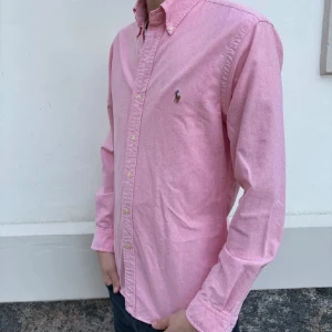 Ralph lauren skjorta  - Hej! Säljer en klassisk rosa skjorta från Ralph Lauren med broderad logga på bröstet. Skjortan har slim fit-passform, knappar hela vägen och lång ärm. Perfekt för en stilren look.