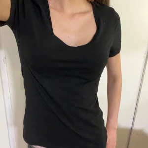 Svart t-shirt med v-ringning - En enkel svart t-shirt med djup v-ringning och korta ärmar. Perfekt basplagg som passar till det mesta. Köptes för två år sedan ungefär men har inte kommit till användning. Toppen är lite figursydd vilket ger en väldigt bra passform. 