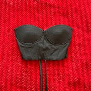 Svart korsett-topp med snörning - Säljer en svart axelbandslös korsett-topp med vadderade kupor och snygg snörning i ryggen. Perfekt att styla till jeans eller kjol för en trendig look.