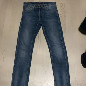 Nudie jeans - Säljer ett par blå jeans med normal passform och raka ben. Jeansen har fem fickor, dragkedja och knapp framtill. Perfekta för en avslappnad stil och funkar året runt.