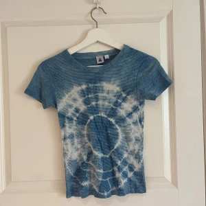 Blå tie-dye t-shirt - Säljer en blå t-shirt med vitt tie-dye mönster. T-shirten har rund halsringning och korta ärmar. Perfekt för en avslappnad och trendig stil.