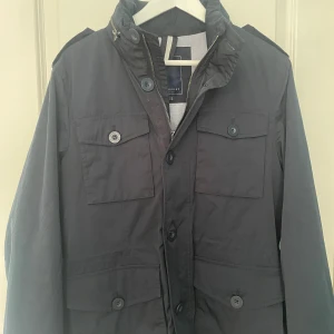 Mörkblå jacka från Berkeley - Säljer en mörkblå jacka från Berkeley med fyra framfickor och både dragkedja och knappar framtill. Jackan har hög krage och axelklaffar för en stilren look. Perfekt för dig som vill ha en klassisk och snygg jacka. Storlek är s men passar m också. Nypris 1700 säljer för 900, pris kan diskuteras. Skick 9/10