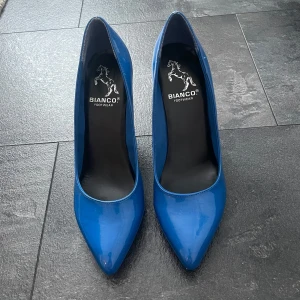 Blåa pumps från Bianco - Säljer ett par stilrena blåa pumps från Bianco med spetsig tå och hög klack. Skorna har en glansig finish och klassisk design som passar perfekt till dig som vill sticka ut lite extra.