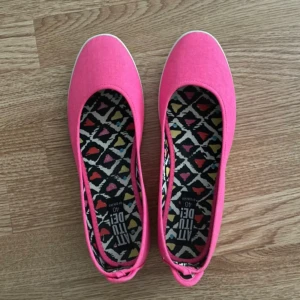 Rosa ballerinaskor från Attitude - Säljer ett par rosa ballerinaskor från Attitude med vit kant runt sulan. Skorna har ett färgglatt, mönstrat innerfoder i olika färger. Perfekta för dig som vill ha något färgstarkt och bekvämt.