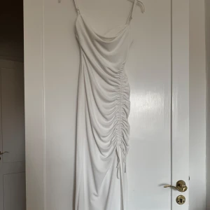 Vit långklänning med slita från Zara - Säljer en elegant vit långklänning från Zara med smala axelband och snygg drapering samt knytning på sidan. 