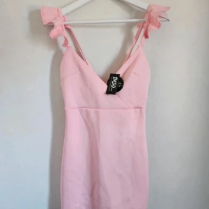 Ljusrosa kortklänning med volangaxelband - Supersöt ljusrosa kortklänning från Ismo med volangdetaljer på axelbanden och djup v-ringning. Klänningen har en figurnära passform och är perfekt för sommarens alla tillfällen. Materialet är mjukt och stretchigt🩷