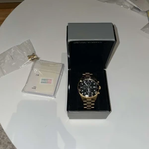 Guldfärgad kronografklocka från Emporio Armani - Snygg herrklocka från Emporio Armani med guldfärgad länk och svart urtavla. Klockan har kronograf och tydliga index, samt levereras i originalask med äkthetsintyg.
