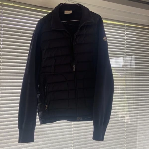 Moncler Cardigan  - Svart Moncler Cardigan med quiltad front och stickade ärmar. Jackan har dragkedja framtill och Moncler-logga på ärmen. Använd två ggr och säljer då den är för stor.