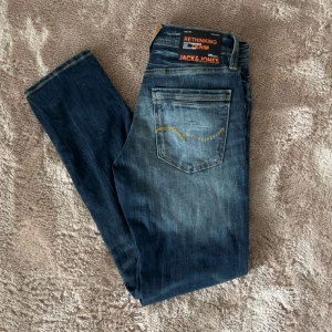 Blå slim fit jeans från Jack & Jones - Snygga blå jeans från Jack & Jones i modellen SLIM/GLENN. Jeansen har klassisk femficksdesign, orangea detaljer och en slim passform. Perfekta för dig som gillar en smalare siluett och slitna tvättade detaljer. Har inte använts. Köpta för 800. W28 L30