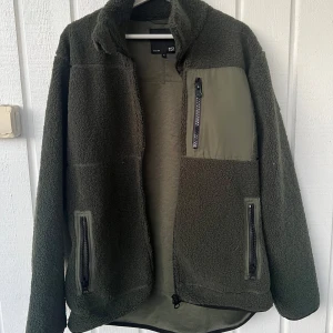 Grön fleecejacka från Lager 157 - Mysig grön fleecejacka med dragkedja framtill och tre fickor med dragkedja. Bröstficka i kontrasterande material. Perfekt för kyliga dagar och enkel att matcha med det mesta. —— Aldrig använd, fick den av en familjekompis men den är för stor för mig.