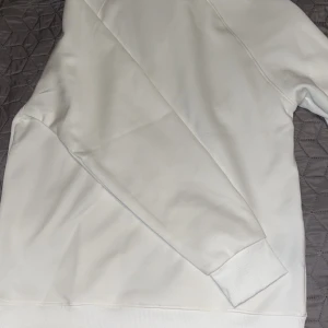 Vit halvzip sweatshirt från Polo Ralph Lauren - Säljer en fräsch vit sweatshirt från Polo Ralph Lauren med halv dragkedja och klassisk gul broderad logga på bröstet. Tröjan har långa ärmar och ribbade muddar. Perfekt för en clean och stilren look. Helt ren. 