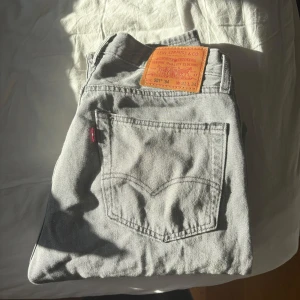 Gråa Levi's 501 jeans - Säljer ett par klassiska gråa Levi's 501 jeans med raka ben och femficksmodell. Jeansen har den ikoniska läderpatchen bak i midjan och röd Levi's-tagg på bakfickan. Perfekta för dig som gillar en tidlös och avslappnad stil. Dom är knappt använda 