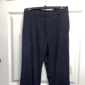 Svarta kostymbyxor från 157 - Svarta kostymbyxor från 157 med klassisk passform och vida ben. Det saknas en liten grej när man knäpper dom men de finns en kvar så det går o knäppa, men det syns inte när dom sitter på. Det ser ut som att dom är lite bootcut där nere vid benen.💞obs har aldrig använd dom, ända skavanken är 1 av 2 fästerna som gått av!