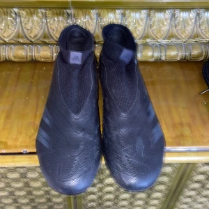 Svarta Adidas Predator fotbollsskor - Säljer ett par svarta Adidas Predator fotbollsskor med strumpliknande skaft och mönstrad ovandel. Skorna har dobbar för spel på gräs och diskreta ränder på sidan. Perfekta för dig som vill ha bra grepp och kontroll på planen. Nypris runt 1000🙌.  Ingen låda
