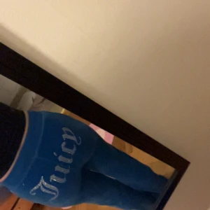 Blå velourbyxor från Juicy Couture - Supersnygga och bekväma byxor i mjuk blå velour från Juicy Couture. Klassisk design med snörning i midjan och den ikoniska “Juicy” texten baktill i skimrande stenar. Även loggan framtill är dekorerad med gnistrande stenar. Endast använda en gång – säljes då de tyvärr är för stora för mig
