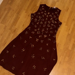 Vinröd klänning med paljetter - Vinröd ärmlös klänning dekorerad med glittriga paljetter. Klänningen har en feminin passform och rund halsringning. Perfekt för speciella tillfällen när du vill sticka ut lite extra.