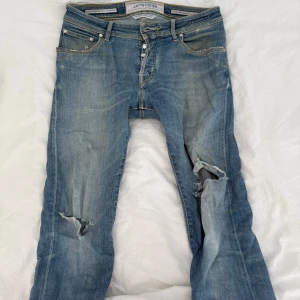 Jacob Cohen jeans - Säljer ett par blå jeans från Jacob Cohen med slitningar och hål på båda benen. Dem är inte i ett jättebra skick o därför är det för ett billigare pris, dem har blivit sydda i mellan benen pga hål som fixades. 