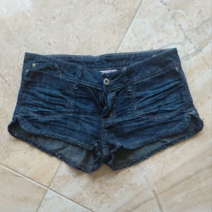 Lågmidjade jeansshorts från Tally Weijl - Snygga lågmidjade mörkblå jeansshorts från Tally Weijl med klassisk design och knapp- samt dragkedjestängning. Shortsen har låg midja och korta ben, perfekta för varma dagar.