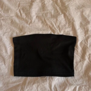 Svart ribbad tubtopp - Säljer en svart ribbad tubtopp som är perfekt att styla till olika outfits. Enkel och stilren design utan axelband, passar bra till både jeans och kjol.