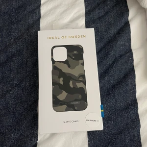 Mattsvart kamouflage mobilskal från iDeal of Sweden - Säljer ett snyggt mobilskal med matt camo-mönster från iDeal of Sweden. Passar till iPhone 13. Skalet har en stilren design i svart, grått och grönt och är gjort i plast. Perfekt för dig som vill ha ett trendigt och skyddande skal. Helt nytt och oöppnat