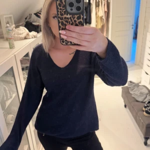 Mörkblå stickad tröja - Mysig mörkblå stickad tröja med v-ringning och långa ärmar. Tröjan har en ribbad struktur som ger en snygg och enkel look. Perfekt att matcha med jeans eller kjol.