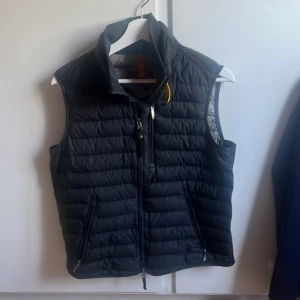 Svart dunväst Super Lightweigh har två små hål annars bra sik - Säljer en svart dunväst från Super Lightweight med quiltad design och dragkedja framtill. Västen har två snedställda fickor med dragkedja och en hög krage. Perfekt för lager-på-lager under kyliga dagar.