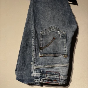Dondup jeans - Säljer ett par blå jeans med slitningar och hål på framsidan. Jeansen har raka ben, klassiska bakfickor och detaljerade sömmar. Perfekta för en avslappnad och trendig look. Skriv om du har några frågor.