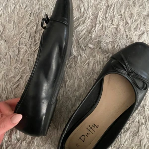 Svarta ballerinaskor  - Säljer ett par klassiska svarta ballerinaskor från Duffy med rund tå och liten rosett framtill. Endast använda fåtal gånger! Följer med kartong.