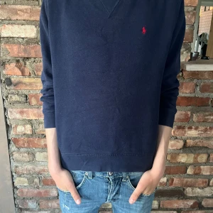Mörkblå sweatshirt från Polo Ralph Lauren - Säljer en klassisk mörkblå sweatshirt från Polo Ralph Lauren med den ikoniska röda loggan broderad på bröstet. Tröjan har rund halsringning och långa ärmar. Perfekt för en stilren och avslappnad look. Den är i L barn så passar om du e runt 160