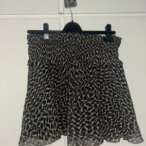 Svartvit mönstrad kortkjol från H&M - Säljer en svartvit kortkjol från H&M med elastisk midja och abstrakt mönster. Kjolen är luftig och har en lätt volang nertill, perfekt för dig som gillar en bekväm och trendig stil.