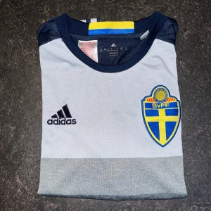 Svensk landslagströja stl 164 - Säljer en landslags fotbollströja från Adidas med svenska flaggan på ärmen. Perfekt för dig som vill visa ditt stöd för Sverige! 