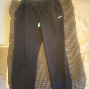 Svarta mjukisbyxor från BOSS - Säljer ett par svarta mjukisbyxor från BOSS med dragsko i midjan och diskret logga på ena benet. Perfekta för en avslappnad stil och riktigt sköna att ha på sig. Klassisk passform och mjukt material.