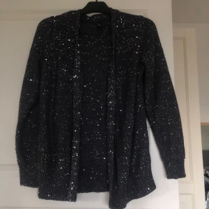 Svart stickad kofta med paljetter från Freequent - Säljer en svart stickad kofta från Freequent, täckt med små paljetter som ger ett glittrigt intryck. Koftan har lång ärm och öppen front, perfekt för att lyfta vilken outfit som helst till fest eller vardag!! Har aldrig använt så den är helt ny! Storlek L och köpte för ett tag sen för 450kr! Skriv vid frågor eller funderingar💓
