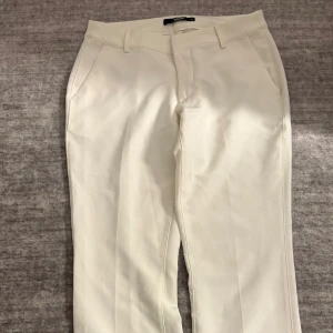 Vita kostymbyxor  - Vita kostymbyxor strl 40  Snygga vita kostymbyxor med slits nertill. Perfekta till studenten! Har en liten fläck från studentflaket som inte går bort, men den syns knappt när man har dem på. Säljes för 100 kr.
