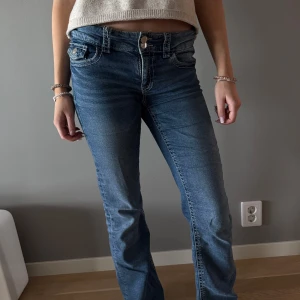 Blå låg midjade jeansbyxor med normal passform - Säljer ett par klassiska blå lågmidjade jeansbyxor med normal passform och raka ben. Byxorna har fem fickor, knapp- och dragkedjegylf samt tydliga sömmar. Perfekta till vardags och enkla att matcha med olika toppar.