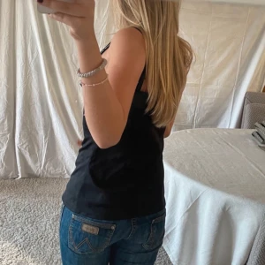 Svart linne med satin detalj  - Säljer en enkel och stilren svart tubtopp. Perfekt att matcha med jeans eller kjol för en clean look. Toppen är ärmlös och har en tight passform.