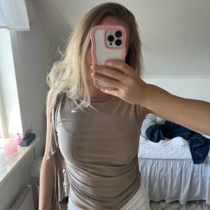 Beige topp från Gina Tricot - Säljer en beige topp från Gina Tricot med snygga rynkade detaljer på sidan och volang längs axeln. Topp i mjukt, stretchigt material som sitter snyggt på kroppen🙌🏼🩷