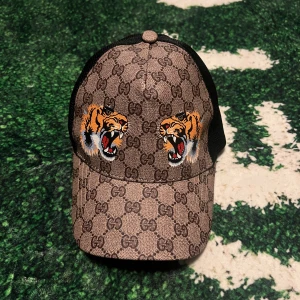 GG keps med tigerbrodyr - Snygg keps från klassiskt GG-mönster i beige och brunt. Framtill finns två broderade tigrar. Kepsen har svart mesh på sidorna och baksidan för extra ventilation. Perfekt accessoar för att sticka ut. Vid funderingar skriv!!! Vid snabb affär bättre pris