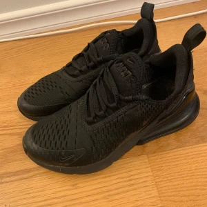 Svarta Nike Air Max 270 sneakers - Säljer ett par helsvarta Nike Air Max 270 sneakers med mesh-ovandel och synlig Air Max-dämpning i hälen. Skorna har snörning och en sportig, modern look. Perfekta för dig som gillar stilrena och bekväma sneakers.